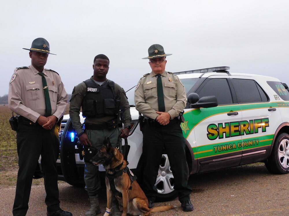 Officers and Blade pose in front of a police vehicle.