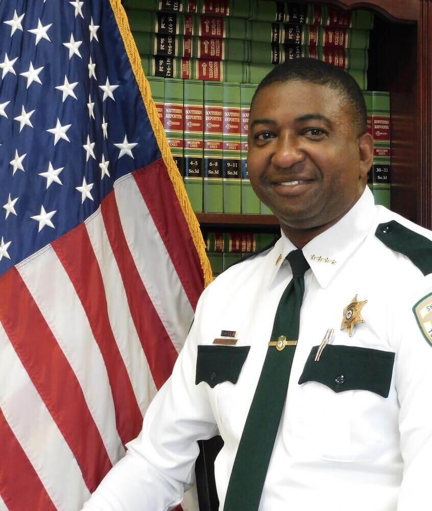 Chief Deputy Eugene Bridges standing next to the Flag of the United States of America.