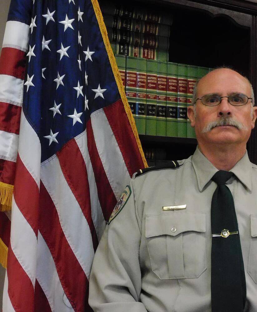 Major Alec Clark standing next to the Flag of the United States of America.