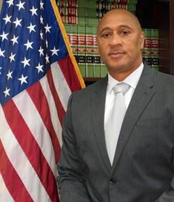 Warden Reginald Boykin standing next to the Flag of the United States of America.