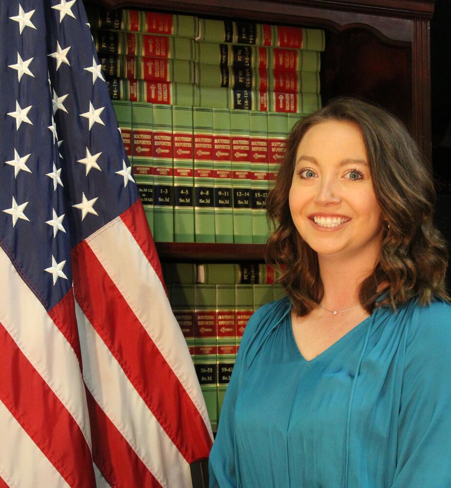 Clara Cupples poses with book case next to American flag for photo