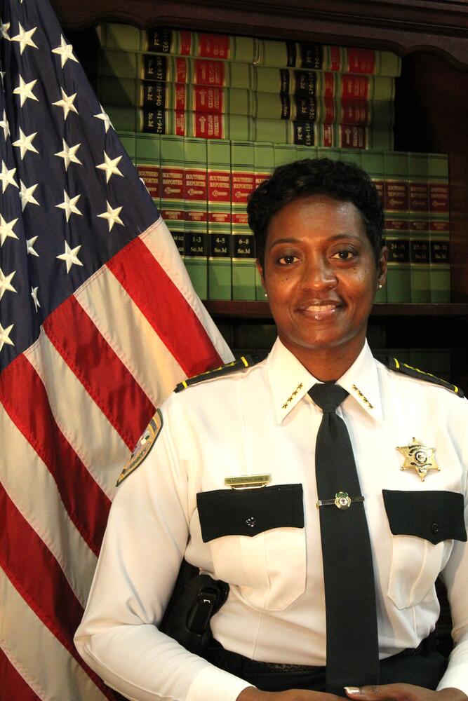 Commander Persundra Jones standing next to the Flag of the United States of America.