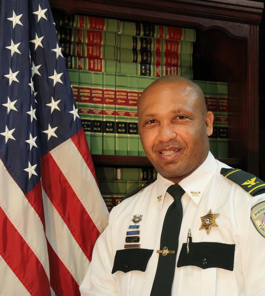 Commander Dennis Hopson standing next to the Flag of the United States of America.